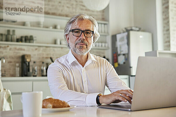 Reifer Geschäftsmann mit grauen Haaren arbeitet in der Cafeteria am Laptop