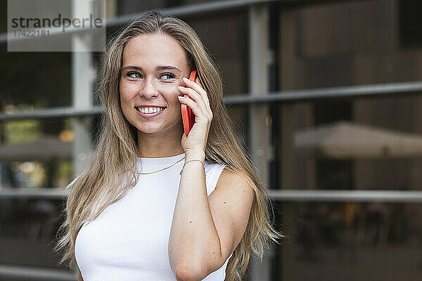 Lächelnde Geschäftsfrau mit langen blonden Haaren  die auf dem Smartphone spricht