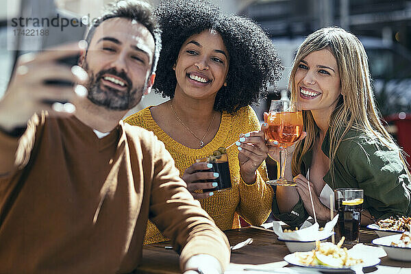 Bärtiger Mann macht Selfie mit Freundinnen  die im Restaurant etwas trinken