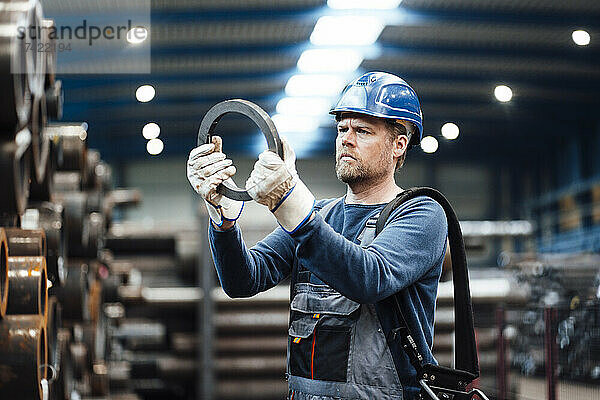 Männlicher Inspektor mit Helm überprüft Stahlausrüstung in der Fabrik