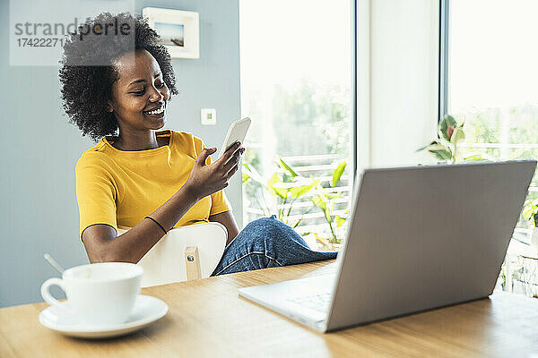 Afro-Fachfrau benutzt Mobiltelefon  während sie zu Hause auf einem Stuhl sitzt