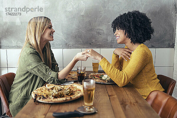 Blonde Frau hält die Hand einer Freundin im Restaurant