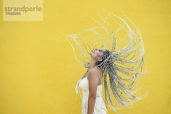 Junge Frau wirft Haare vor gelber Wand