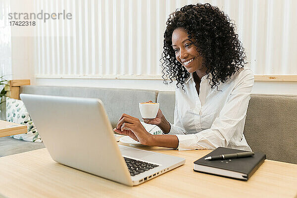 Geschäftsfrau mit Kaffeetasse lächelt bei Videoanruf über Laptop im Café