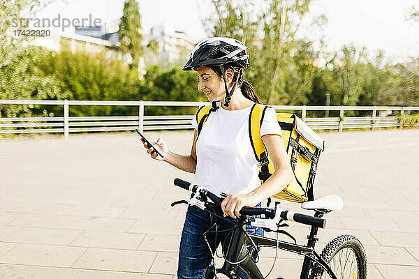 Lächelnde Lieferfrau benutzt Mobiltelefon  während sie Fahrrad fährt