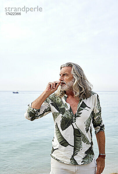 Reifer Mann mit grauen Haaren raucht am Strand in der Nähe des Meeres