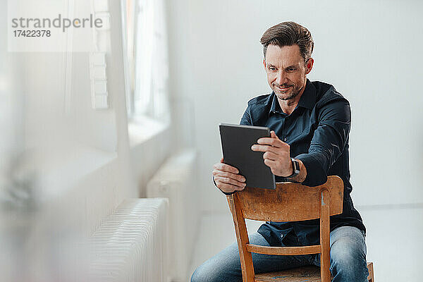 Reifer männlicher Berufstätiger nutzt digitales Tablet  während er im Büro auf einem Stuhl sitzt