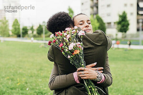 Geschäftsfrau hält Blumenstrauß in der Hand und umarmt Kollegen im Park