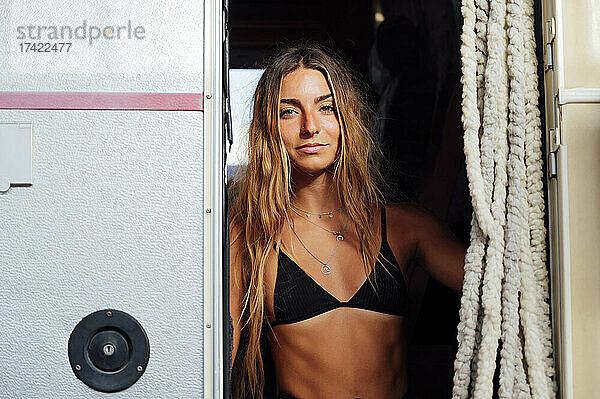 Frau im Bikini steht vor der Tür eines Campingbusses