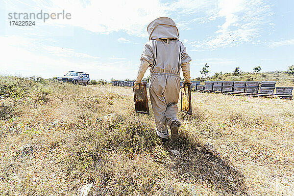 Männlicher Imker mit Bienenstöcken läuft an einem sonnigen Tag durch den Bauernhof