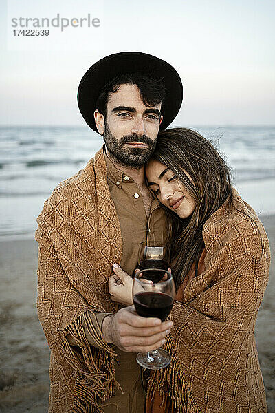 Freund in Decke gehüllt  Freundin hält Wein am Strand