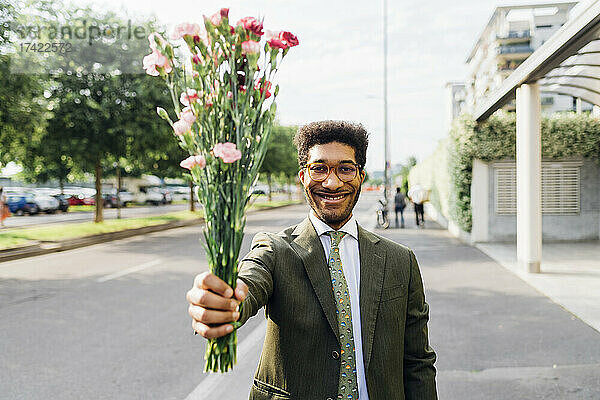 Glücklicher Geschäftsmann zeigt Blumenstrauß  während er auf der Straße steht