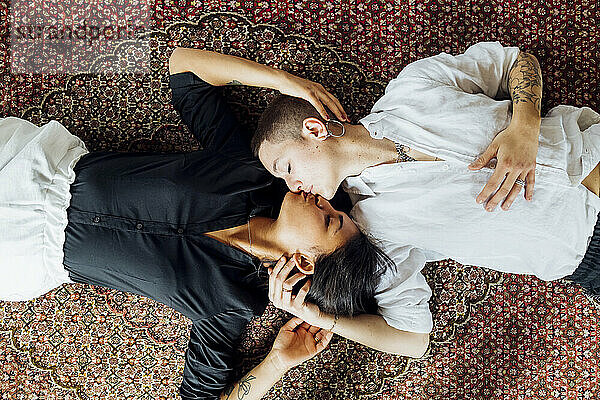 Junge multiethnische Lesben küssen sich  während sie zu Hause auf dem Teppich liegen