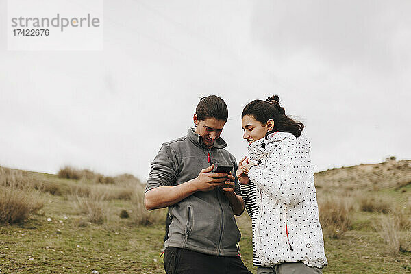 Junger Mann teilt Smartphone mit Freundin im Feld