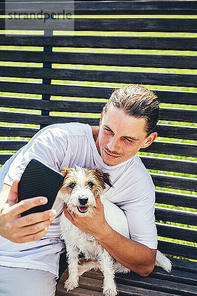 Mann macht Selfie mit Haustier per Handy  während er auf Bank sitzt
