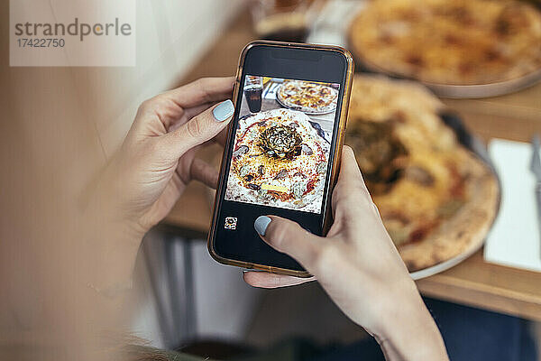 Frau mittleren Alters fotografiert Pizza per Smartphone im Restaurant