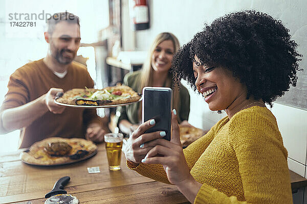 Glückliche Afro-Frau macht ein Selfie mit männlichen und weiblichen Freunden  die im Restaurant Pizza essen