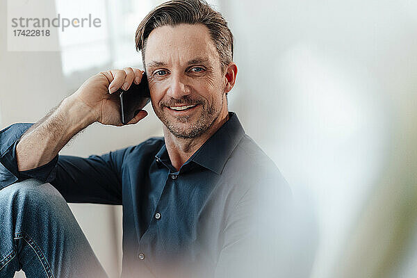 Lächelnder reifer männlicher Berufstätiger  der im Büro mit dem Mobiltelefon spricht