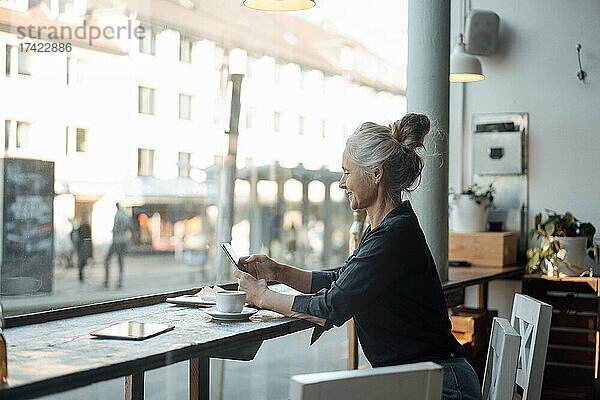 Freiberuflerin benutzt Mobiltelefon  während sie im Café am Glasfenster sitzt