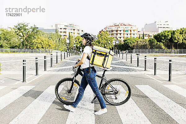 Zustellerin mit Rucksack fährt an sonnigem Tag Fahrrad auf der Straße