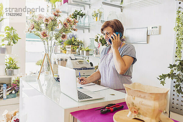 Lächelnde Floristin telefoniert  während sie an der Kasse im Geschäft steht