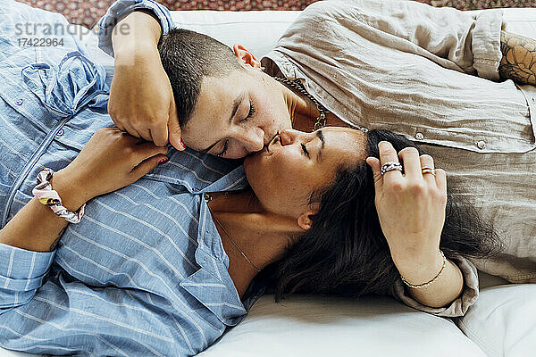 Lesbische Frauen küssen sich  während sie zu Hause zusammen auf dem Sofa liegen