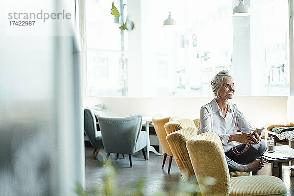 Lächelnde Geschäftsfrau mit Mobiltelefon sitzt auf einem Stuhl im Café