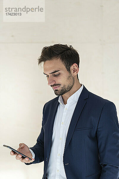 Junger Geschäftsmann schreibt Textnachrichten per Smartphone  während er vor der Wand steht