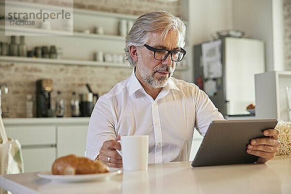 Geschäftsmann mit digitalem Tablet beim Kaffeetrinken in der Bürokantine