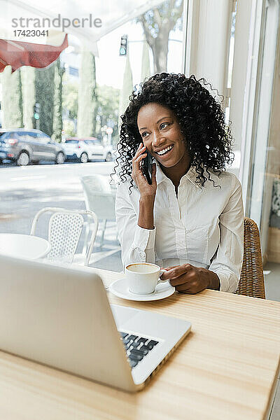 Lächelnde Geschäftsfrau  die im Café mit dem Handy telefoniert