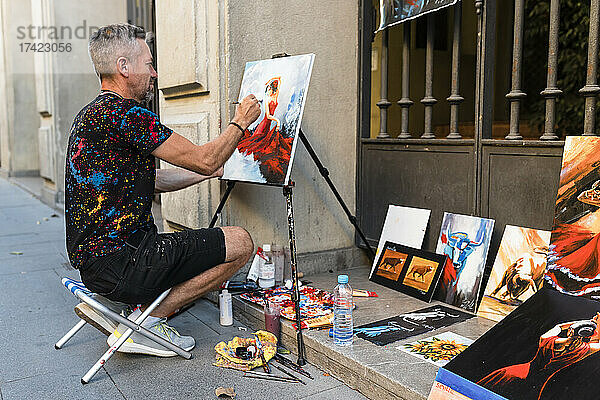 Männlicher Maler malt auf Leinwand  während er auf der Straße sitzt