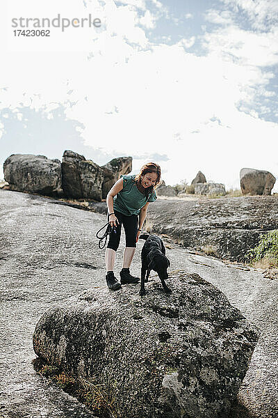 Lächelnde Frau und Hund stehen auf einem Felsen