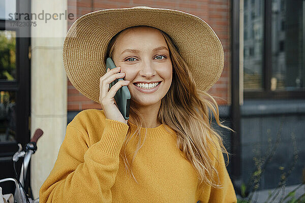 Schöne blonde Frau mit Hut  die auf dem Smartphone spricht