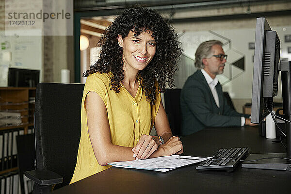 Lächelnde Berufstätige mit Dokumenten am Schreibtisch im Büro