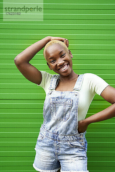 Glückliche junge Frau  die mit der Hand auf der Hüfte vor einer grünen Wand steht