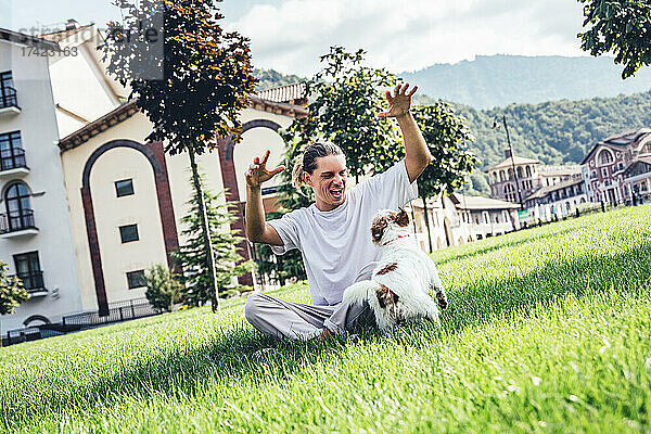 Junger Mann spielt mit Hund  während er im Rasen sitzt
