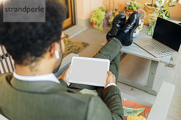 Männlicher Geschäftsprofi nutzt digitales Tablet  während er zu Hause sitzt