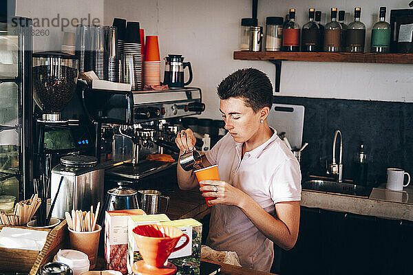 Besitzerin gießt Kaffee in Tasse  während sie im Café arbeitet