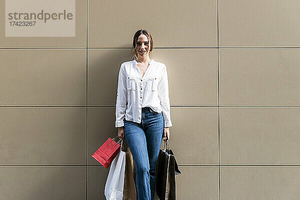 Lächelnde Frau steht mit Einkaufstüten an der Wand