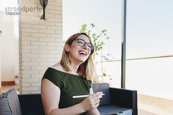 Glückliche Geschäftsfrau mit digitalisiertem Stift sitzt auf dem Sofa auf dem Dach