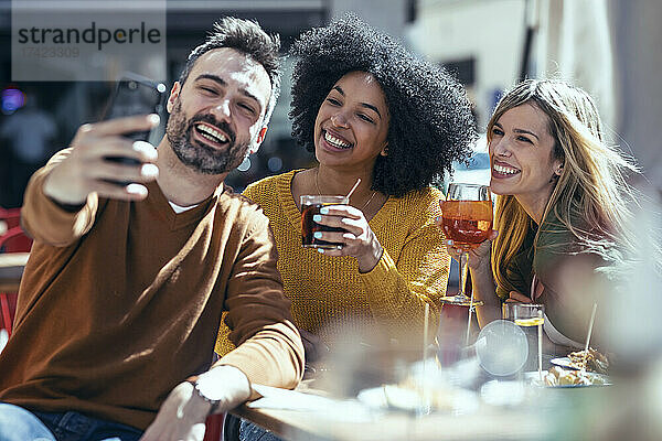 Fröhlicher Mann macht Selfie mit Freundinnen im Restaurant