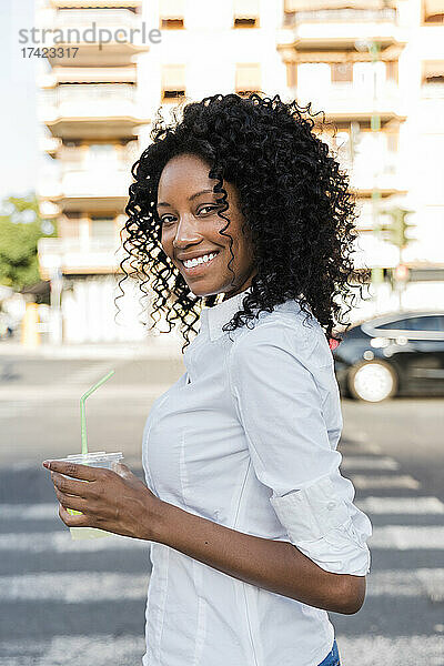Lächelnde Geschäftsfrau hält Saft in der Hand  während sie auf der Straße steht