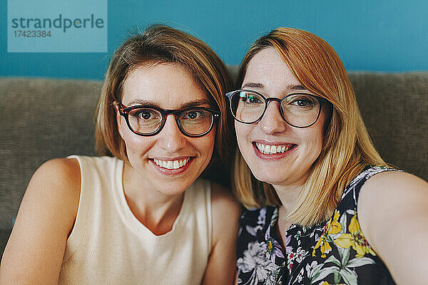 Fröhliche Freiberuflerinnen mit Brillen sitzen zu Hause auf dem Sofa