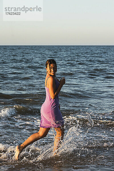 Verspielte Frau spritzt Wasser beim Laufen am Strand