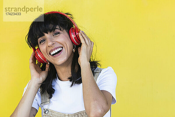Glückliche junge Frau  die vor der gelben Wand Musik hört