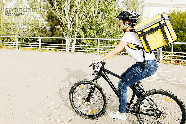Weibliche Zustellerin mit Helm und Rucksack fährt Fahrrad auf der Straße