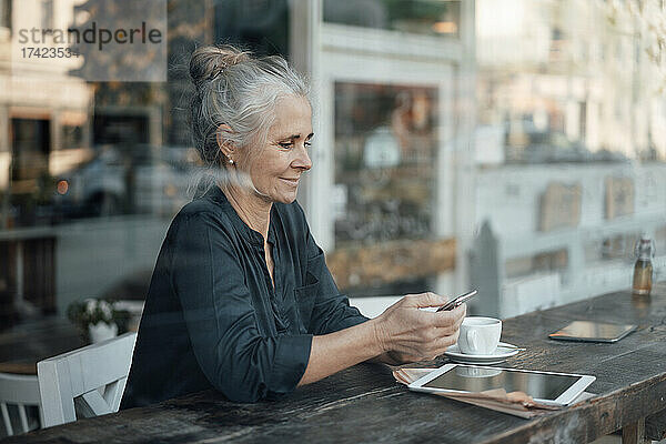 Freiberuflerin benutzt Mobiltelefon  während sie im Café sitzt und durch die Glasscheibe gesehen wird