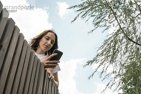 Junge Frau benutzt Mobiltelefon an Stützmauer
