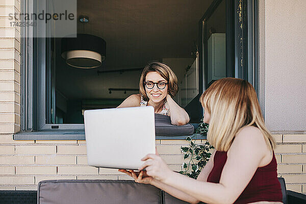 Geschäftsfrau zeigt Laptop einem Kollegen  der am Fenster lehnt