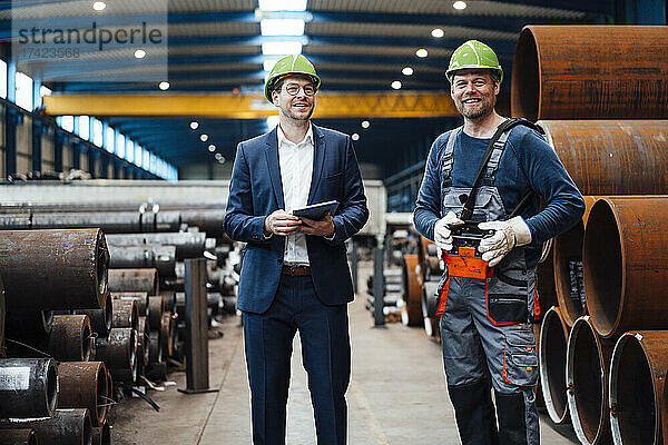 Lächelnder männlicher Manager steht mit Lagerarbeiter in der Fabrik